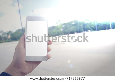 Close up image of a hand holding a white smart phone with a blank white screen. With concrete floor and sky as a background. Technology. Flare near the smart phone.