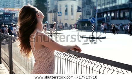 Young woman with long hair look at the street in the city. People pedestrians crossing crosswalk on the background.