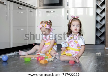 happy sisters children girls bake cookies, knead dough, play with flour and laugh in the kitchen