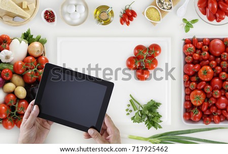 hands with digital tablet above on white cutting board with vegetables and tomatoes food ingredients on kitchen white worktop, copy space, top view