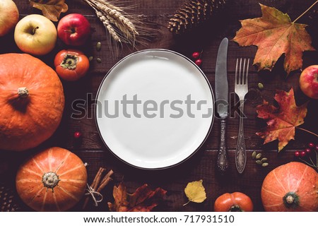 Autumn Halloween or thanksgiving day table setting. Fallen leaves, pumpkins, spices, empty plate and vintage cutlery on wooden table. Thanksgiving background mock up. Top view, toned image