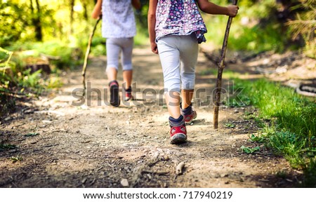 Children hiking in mountains or forest with sport hiking shoes. Girls are walking trough forest path wearing mountain boots and walking sticks. Frog perspective with focus on the shoes. Royalty-Free Stock Photo #717940219