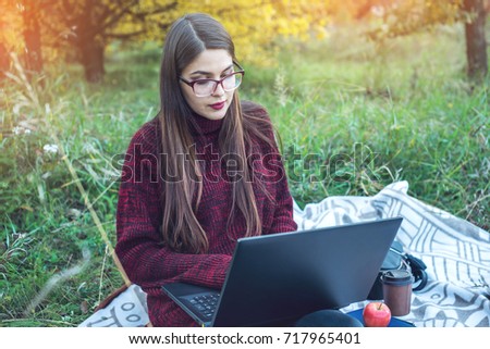 Woman working or studying on laptop wireless printing text. Autumn Park with trees on the background. The concept of education and working with nature