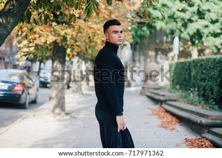 boy in black sweater standing in the street in his hands holding jacket on green background fashion dressed, wrapped behind