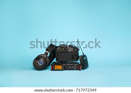 equipment for field video production, camera, boom mic, recorder and wireless system on blue background