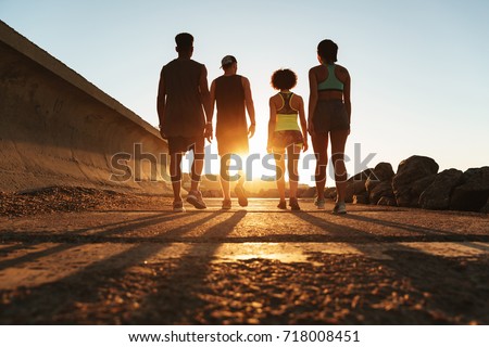 Full length back view image of four fitness people walking outdoors at the beach