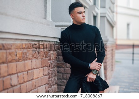 guy in a black jacket and black pants with a clock on his arm spret at the house, fashion dressed