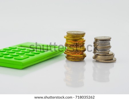 Stack of gold and silver coins with green calculator on white background