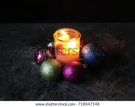 Burning candle in glass holder and colorful decorative Christmas balls on dark background. New year greeting card, poster, advertisement design element.
