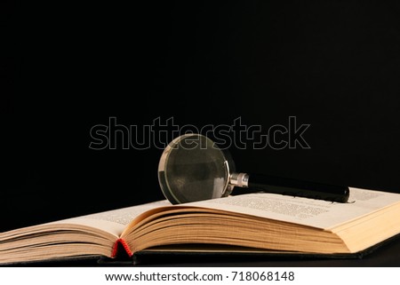 Book and magnifying glass isolated on black background as a symbol of knowledge and science. Search and education concept. 