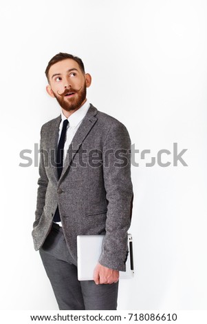 Surprised man with red beard poses in grey suit with tablet in his hand