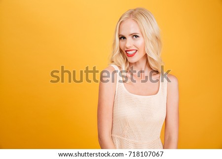 Picture of beautiful young blonde woman standing isolated over yellow wall background. Looking camera.