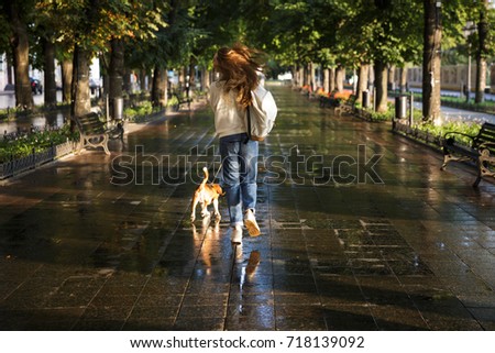 Full length back view image of Brunette woman in autumn clothes walks with dog in park