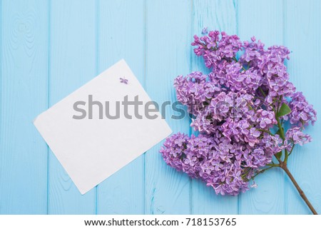 Spring nature background. Branch of purple lilac flowers with white sheet of paper on blue wooden shabby planks. Top view, flat lay, copy space for text