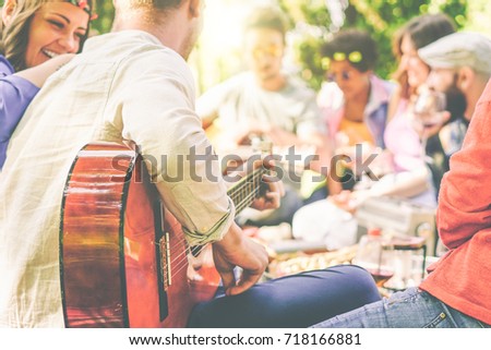 Group of friends having a picnic in a park outdoor - Happy young mates enjoying pic-nic playing guitar, singing and drinking wine eating food - Recreation concept - Focus on man arm's with guitar 