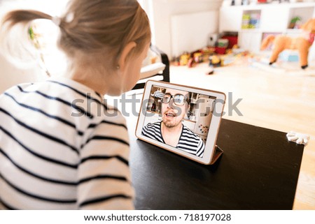Little girl at home with tablet, video chatting with her father.