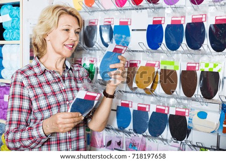 Portrait of mature cheerful woman customer standing next to shelf with textile patches for in a sewing shop 