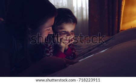 Close-up of mother and her little daughter watching tablet. Cute girl looking at device while chilling at home.