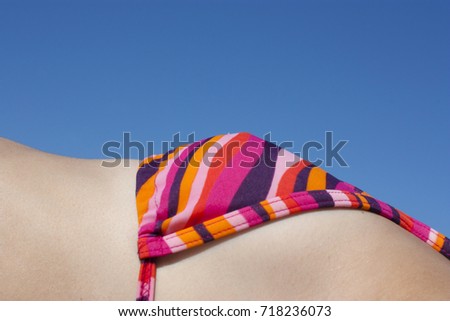 Detail of female body in bikini top sunbathing against the blue sky
