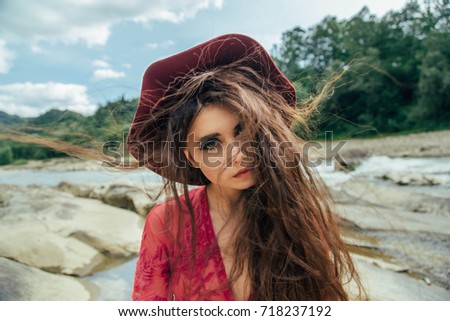 Portrait of a beautiful girl in a red hat. The wind twists her long hair beautifully. Background wild nature. Creative colors.