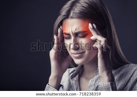 Young woman is suffering from a headache against a dark background. Studio shot Royalty-Free Stock Photo #718238359