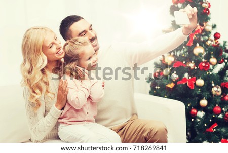 christmas, holidays, technology and people concept - happy family sitting on sofa and taking selfie picture with smartphone at home