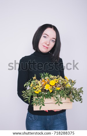 young girl in the image of the florist. holding a crate of flowers. emotional professional portrait. short hair and clean skin. posing in Studio on a white textured background