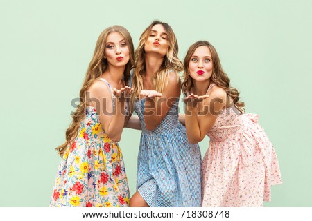 Sending air kiss. Three best friends posing in studio, wearing summer style dress against green background. Girls smiling and having fun. Studio shot on green background