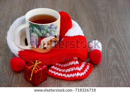 Year of the dog. Tea in a mug with a picture of a dog. New Year's composition. A red knitted scarf warms a cup of tea. A dog in the Santa Claus hat creates a New Year mood in the year of the dog.