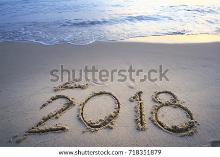 New Year 2018 is coming concept - inscription 2017 and 2018 on a beach sand, the wave is starting to cover the digits 2017