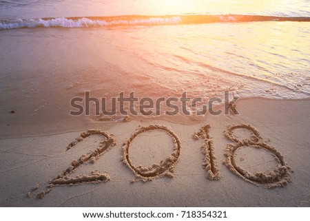 New Year 2018 is coming concept - inscription 2017 and 2018 on a beach sand, the wave is starting to cover the digits 2017 Royalty-Free Stock Photo #718354321