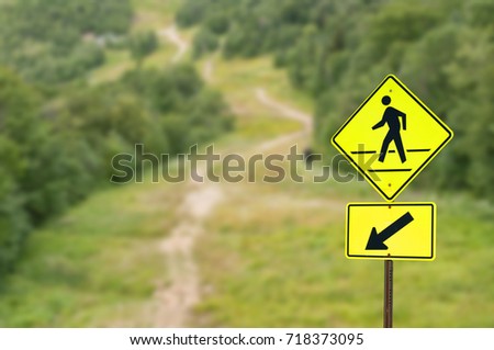 Yellow pedestrian sign against green forest trail background
