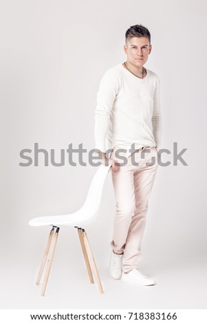  serious young man in white sweater stands near a chair on white background