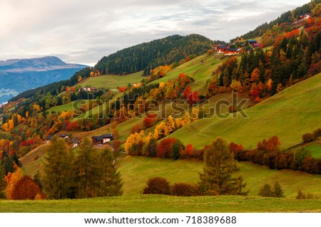 Picturesque autumn morning scenery of colorful trees on mountain hill and mountains on background. Location place: Santa Maddalena, South Tyrol, Dolomite Alps, Italy. Beautiful nature background. Royalty-Free Stock Photo #718389688