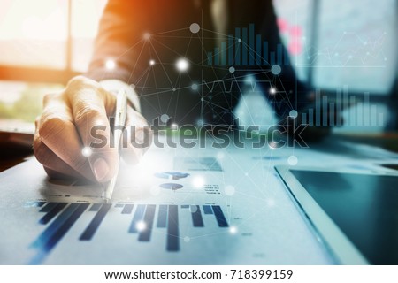 Close up Businessman hand holding pen and pointing at financial paperwork with financial network diagram.  Royalty-Free Stock Photo #718399159