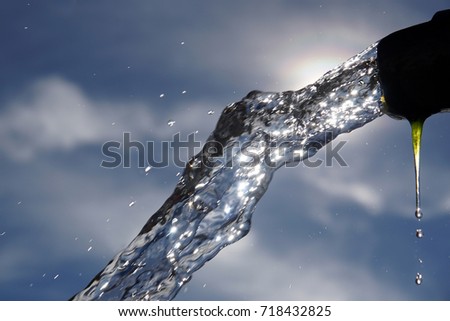 Running water from a metal hole, sky and clouds for background.