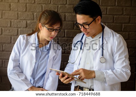 Two Asian medical doctor and assistant colleagues with white lab coat search information on digital tablet to look up patient records and charts for physical analysis. Healthcare and Hospital concept.