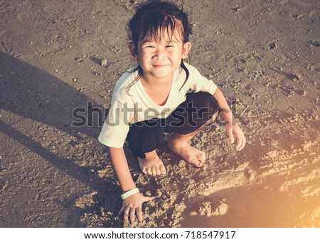 Happy asian child has fun digging in the sand. Charming young girl smiling and looking at camera on the beach. Outdoor with bright sunlight on summer day. Concept of connecting children with nature.