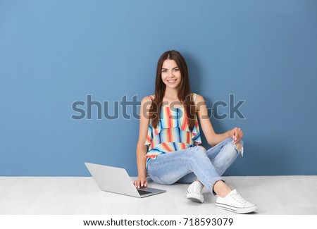 Young woman sitting with laptop near color wall
