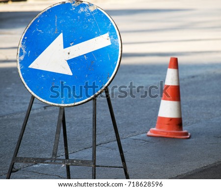 Road sign arrow mandatory direction to the left and traffic cone