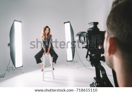 professional photographer and beautiful model on fashion shoot in photo studio with lighting equipment   Royalty-Free Stock Photo #718655110