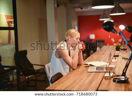 Business blonde girl drinking a cup of coffee in front of a laptop