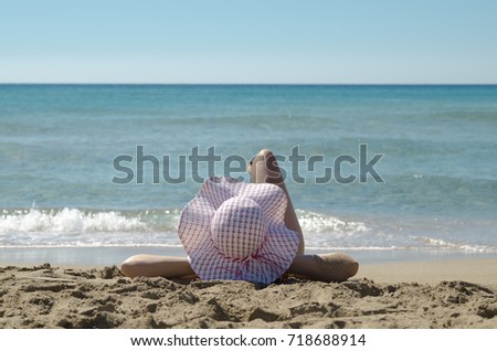 Young woman back head in sun hat laying on sand beach and watch sea water. Hedonism and enjoy. Relax and sun tanning on vacation.