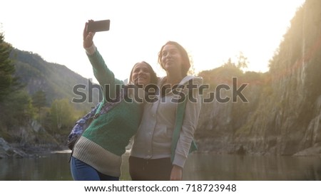Beautiful women is taking selfie on the phone against the background of big mountains and the green mountain river during sunset.