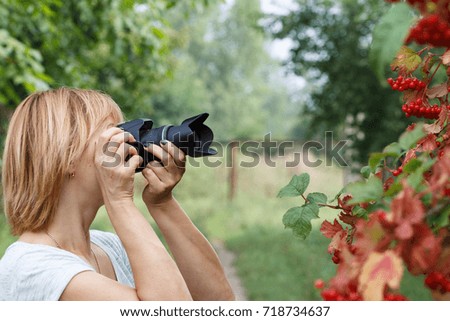 Young woman holding digital camera and taking pictures of viburnum branches outdoors in nature. Healthy active lifestyle