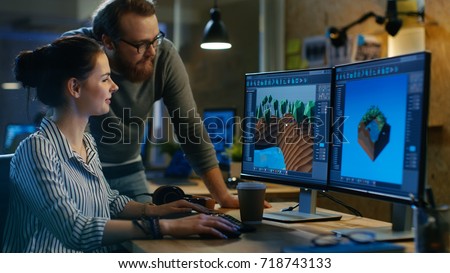 Female Game Developer Has Discussion with Male Project Manager While Working on a Game Level on Her Personal Computer with Two Displays. They Work in a Modern Loft Office Creative Environment. Royalty-Free Stock Photo #718743133