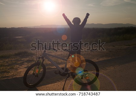 Child enjoying sunset , feeling like a winner, next to his bicycle. Cycling.