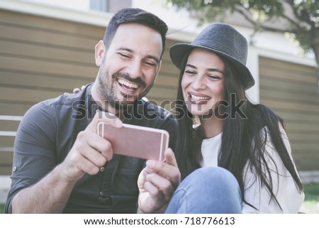 Young couple sitting in city park. Loving couple taking selfie with smart phone. Focus on hands.