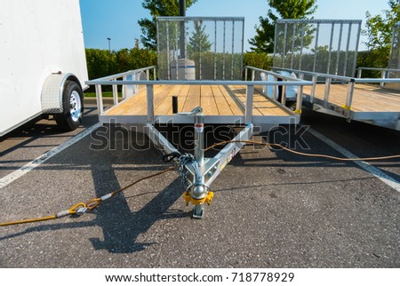 Front View of a Open Flat Bed Utility Trailer Parked Next to a Cargo Trailer Royalty-Free Stock Photo #718778929