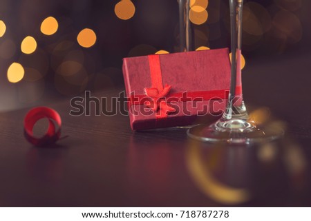Detail of two champagne glasses placed on the table with small nicely wrapped gift box and Christmas tree and lights in the background. Selective focus